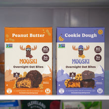 Front of two Mooski Overnight Oat Bites boxes, Peanut Butter and Cookie Dough, 80 cal, 3g sugar, on a refrigerator shelf